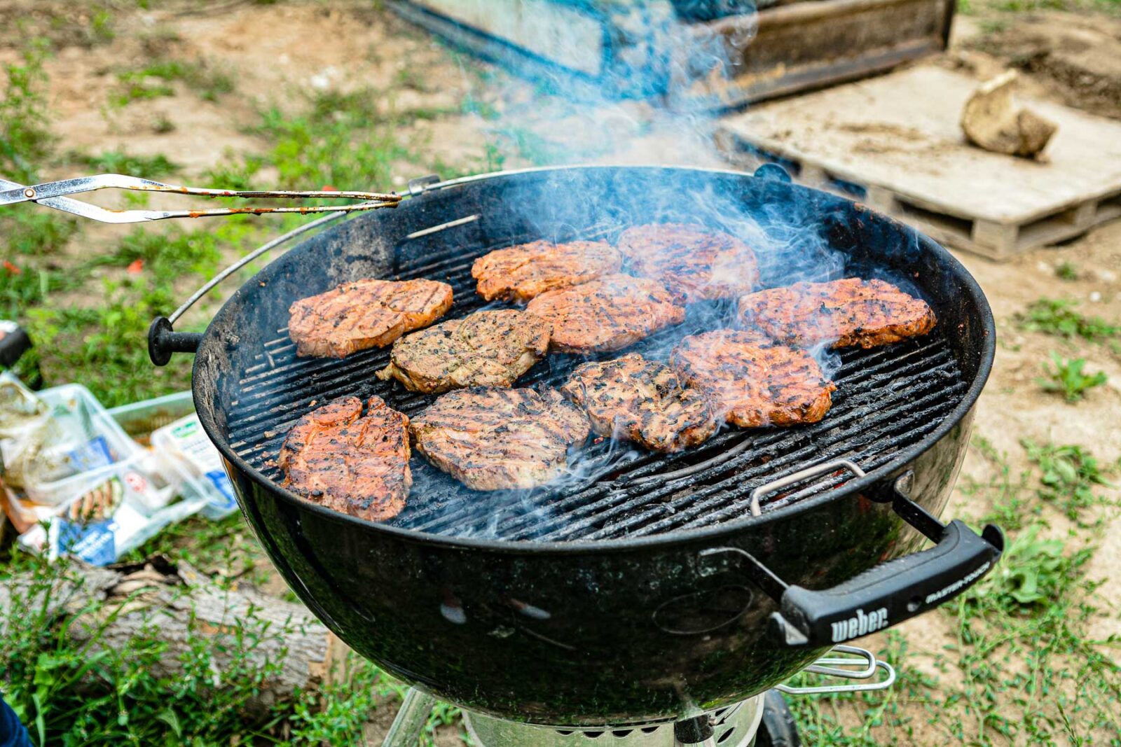 Seasoned meat cooking and smoking on a black charcoal grill.
