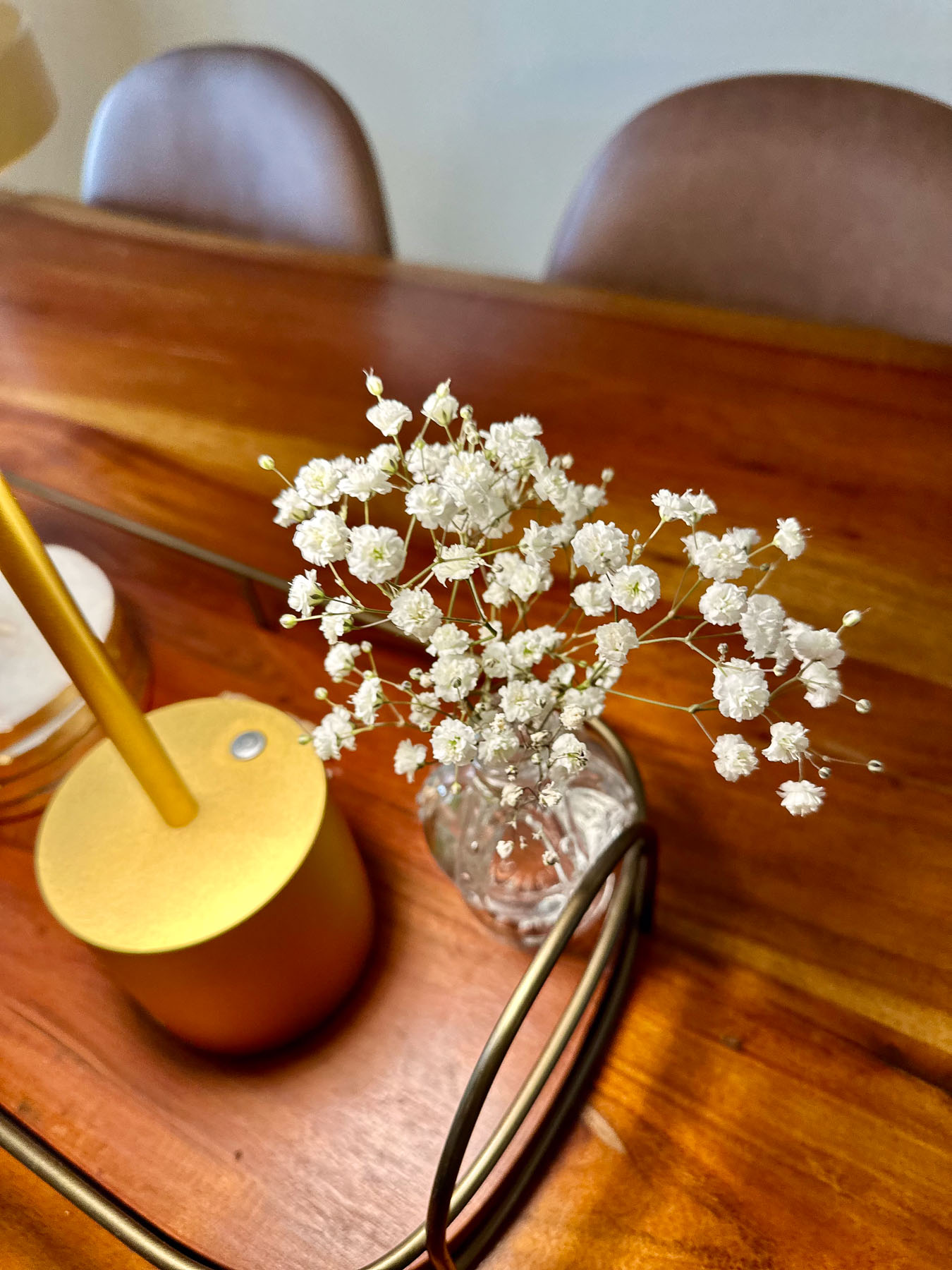 Fresh white baby's breath flowers in a small round glass vase sitting on a wooden table to add a light, airy texture.